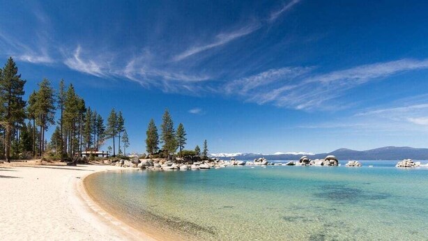 A beach with clear turquoise water, sandy shore, and tall pine trees. - Whispering Pines in Tahoe Vista (Tahoe Vista)