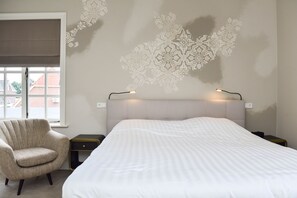 A bedroom with a large bed, a chair, a nightstand, and a wall with a decorative pattern. - Herberg de Zwaan (Elspeet)