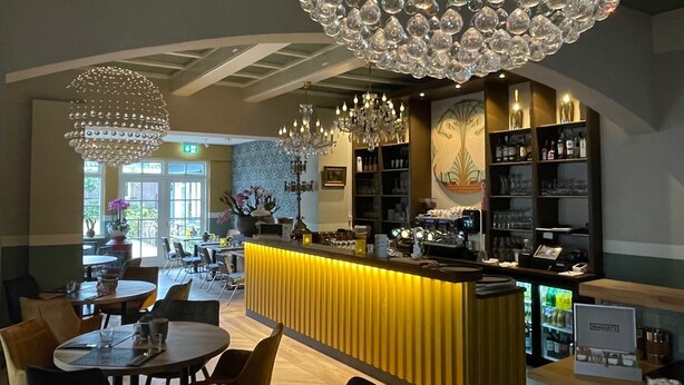 Un restaurant doté d’un bar, de lustres et offrant une vue sur l’extérieur.