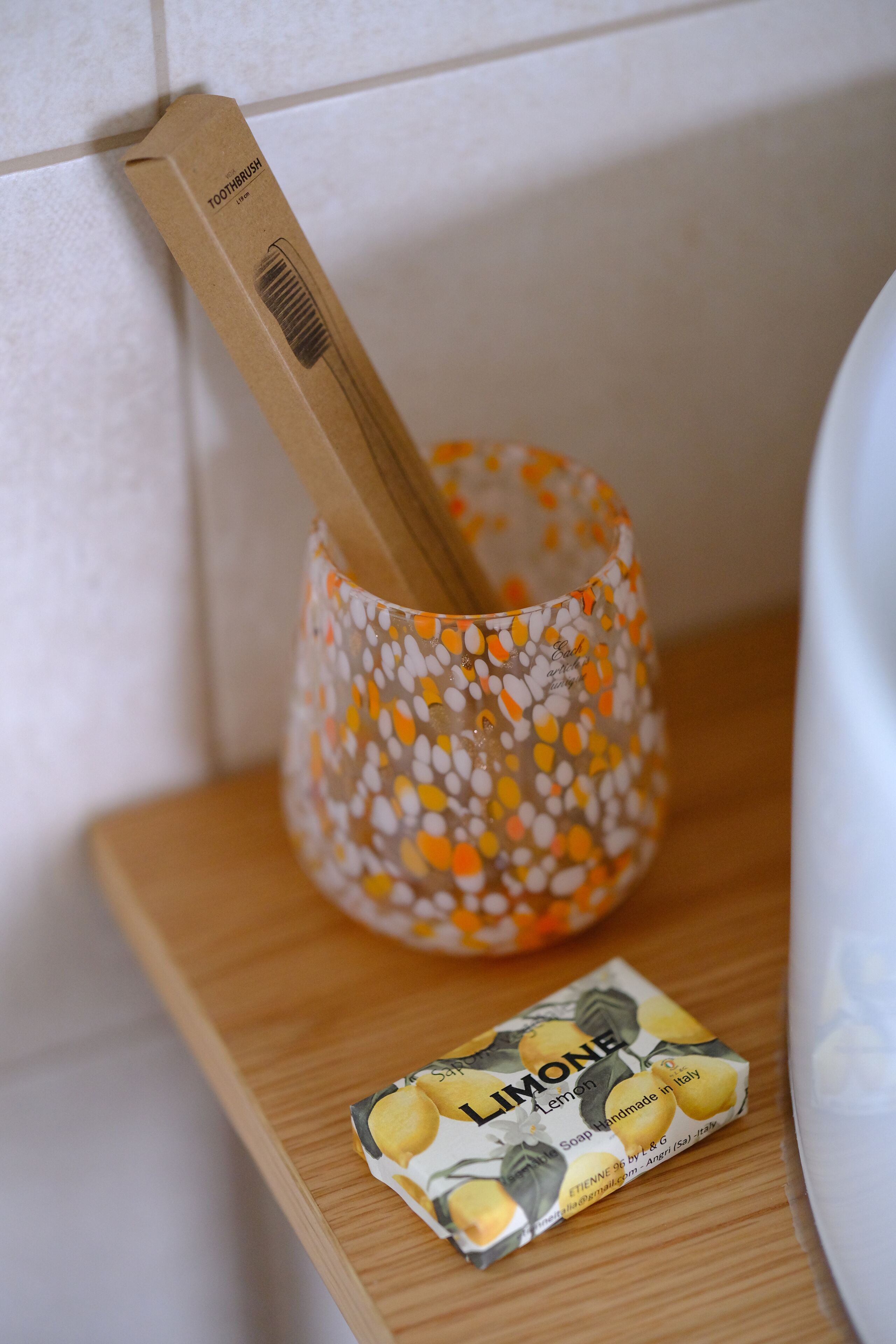 Uno spazzolino in una tazza decorata su un ripiano di legno, vicino a una confezione di sapone al limone.