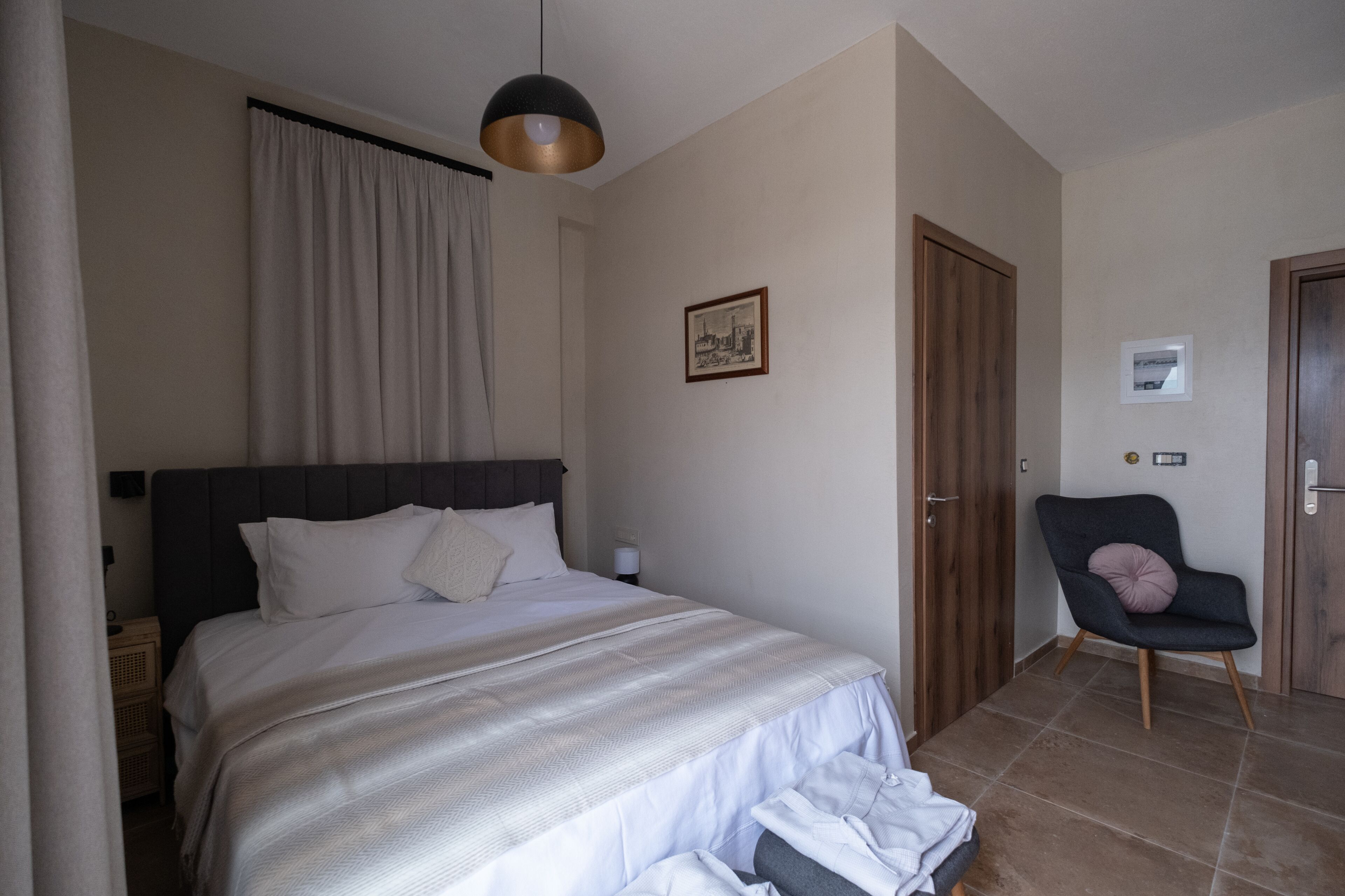 Un dormitorio con cama, una silla, una puerta y un cuadro en la pared.