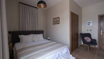 Un dormitorio con cama, una silla, una puerta y un cuadro en la pared.