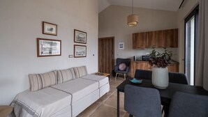 A modern living room with a sofa, dining table, and chairs. There are framed pictures on the wall, a wooden door, and a kitchen area with cabinets and a sink. - blue crystal view (Pangaio)