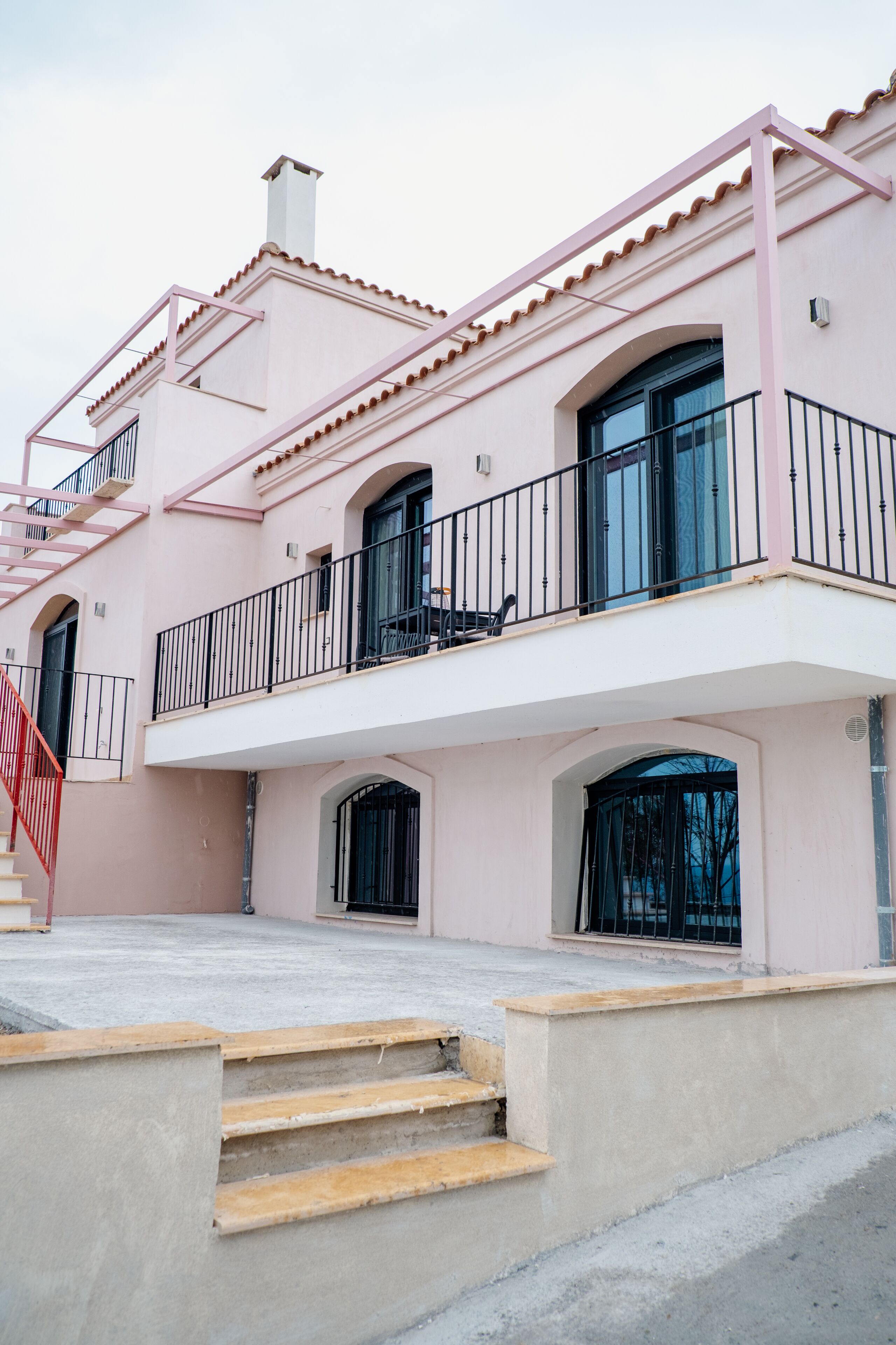 Um edifício rosa de dois andares com varanda, escadaria e chaminé.
