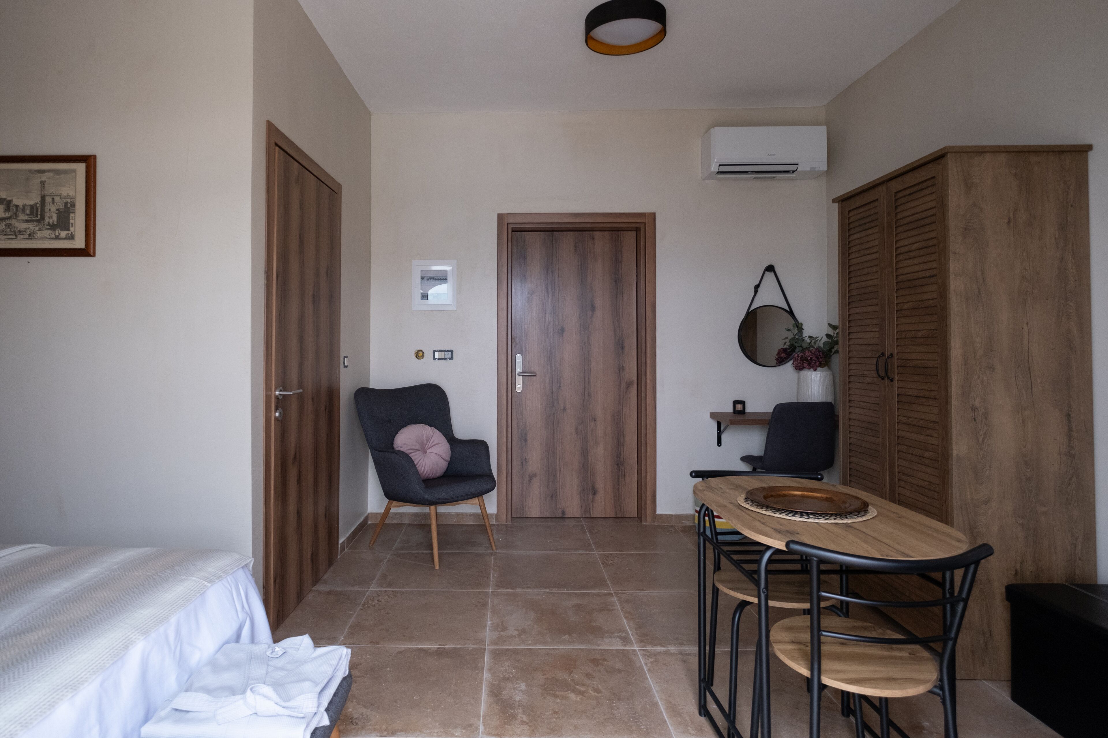 Ein kleines Zimmer mit einem Bett, einem Esstisch mit Stühlen, einem Holzschrank und einer Tür zu einem anderen Raum.
