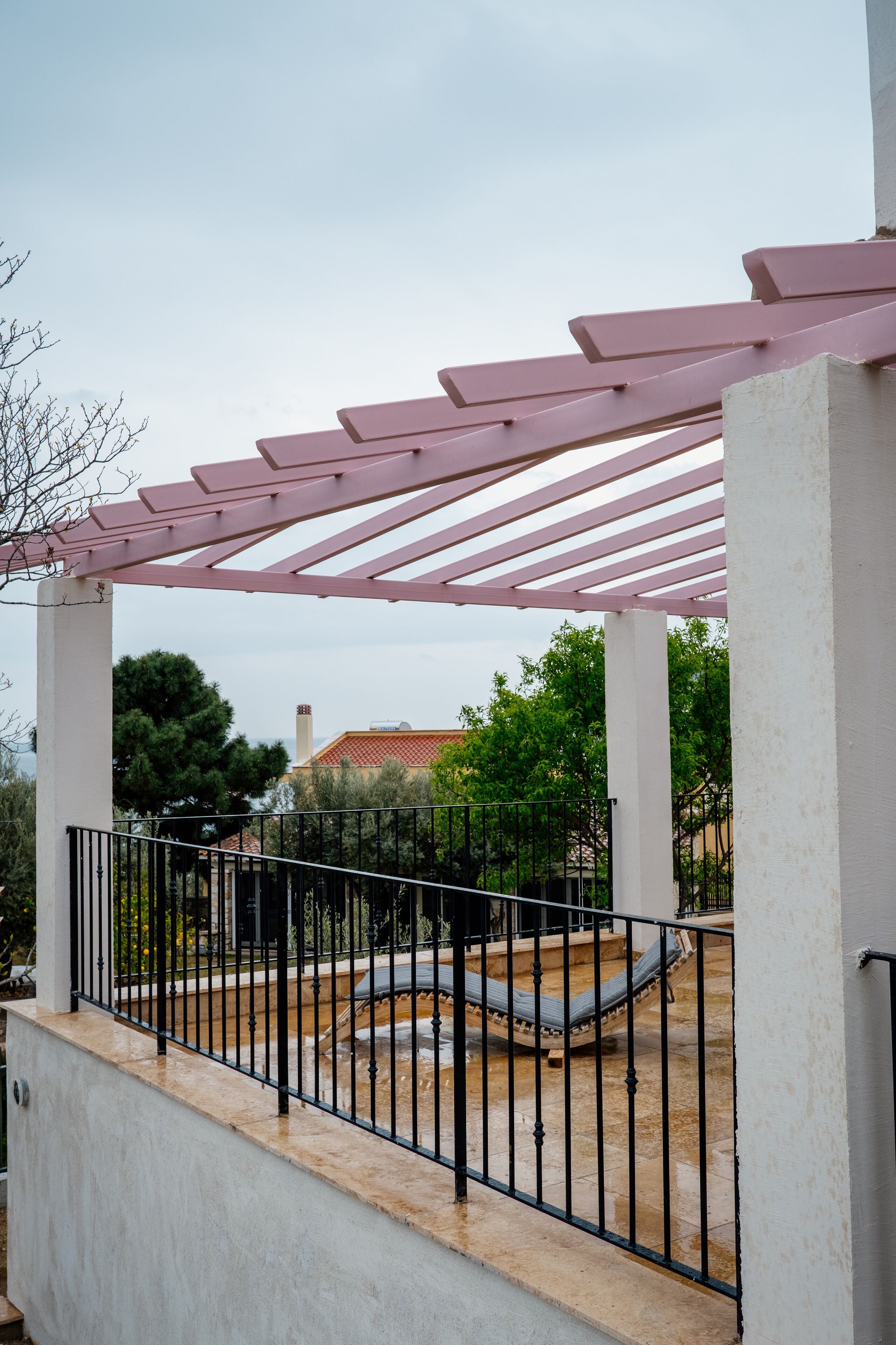 Un espacio exterior cubierto con una pérgola, una pared blanca y una barandilla de metal negro.