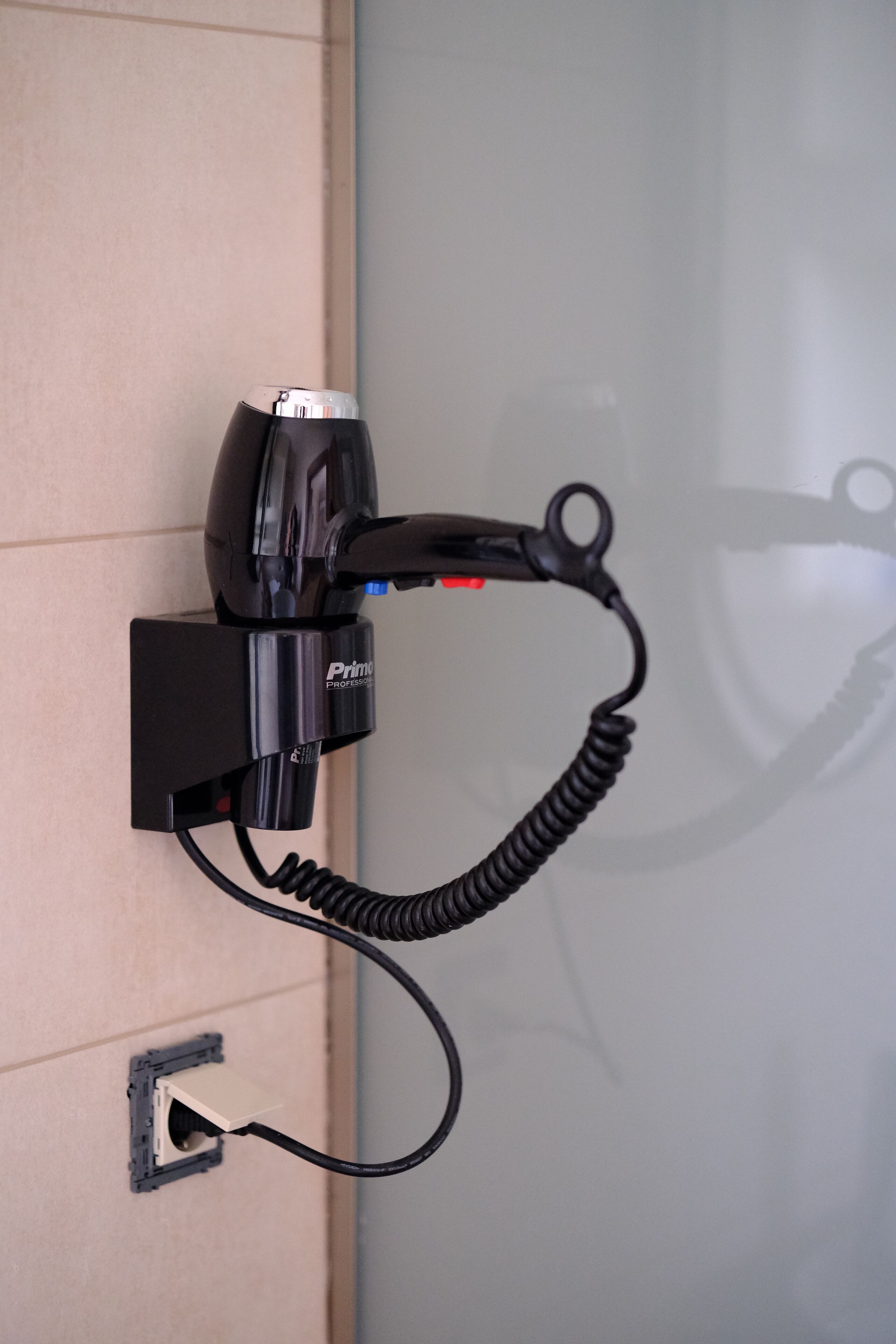 A hair dryer mounted on a wall with a coiled cord.