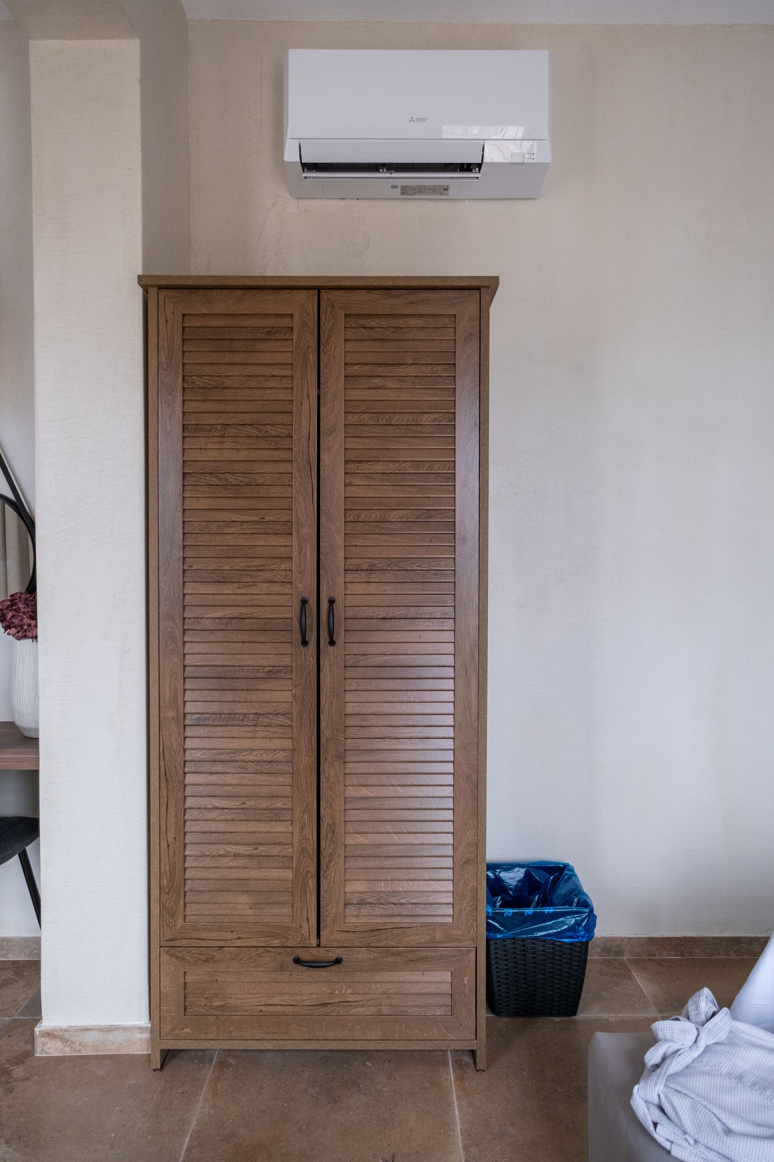 Ein Holzkleiderschrank mit zwei Türen, eine blaue Mülltonne und eine Klimaanlage an der Wand.