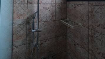 A shower with a handheld showerhead, a wall-mounted faucet, and a handheld showerhead.