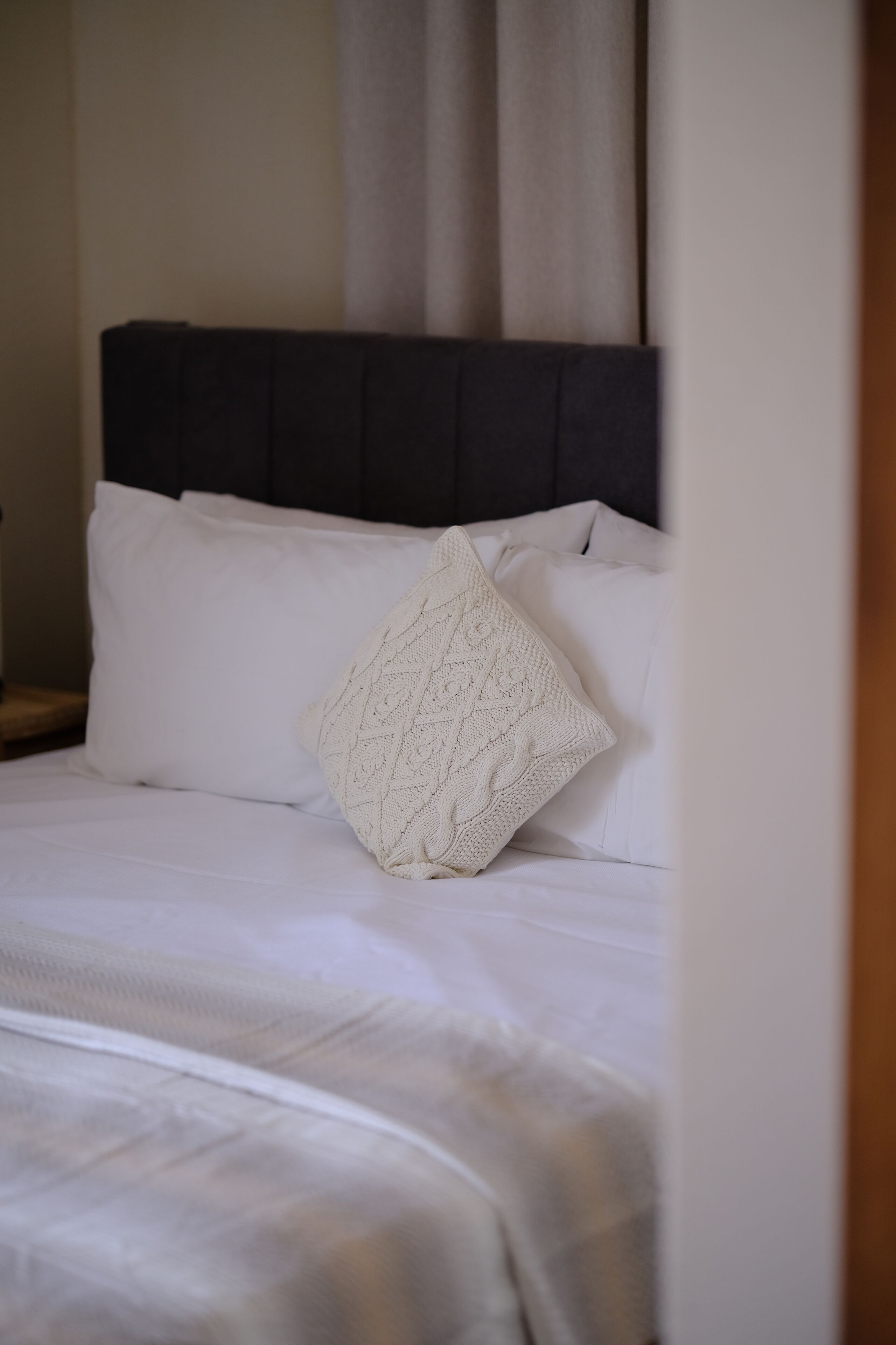 Una cama bien hecha con sábanas blancas y un cojín decorativo tejido.
