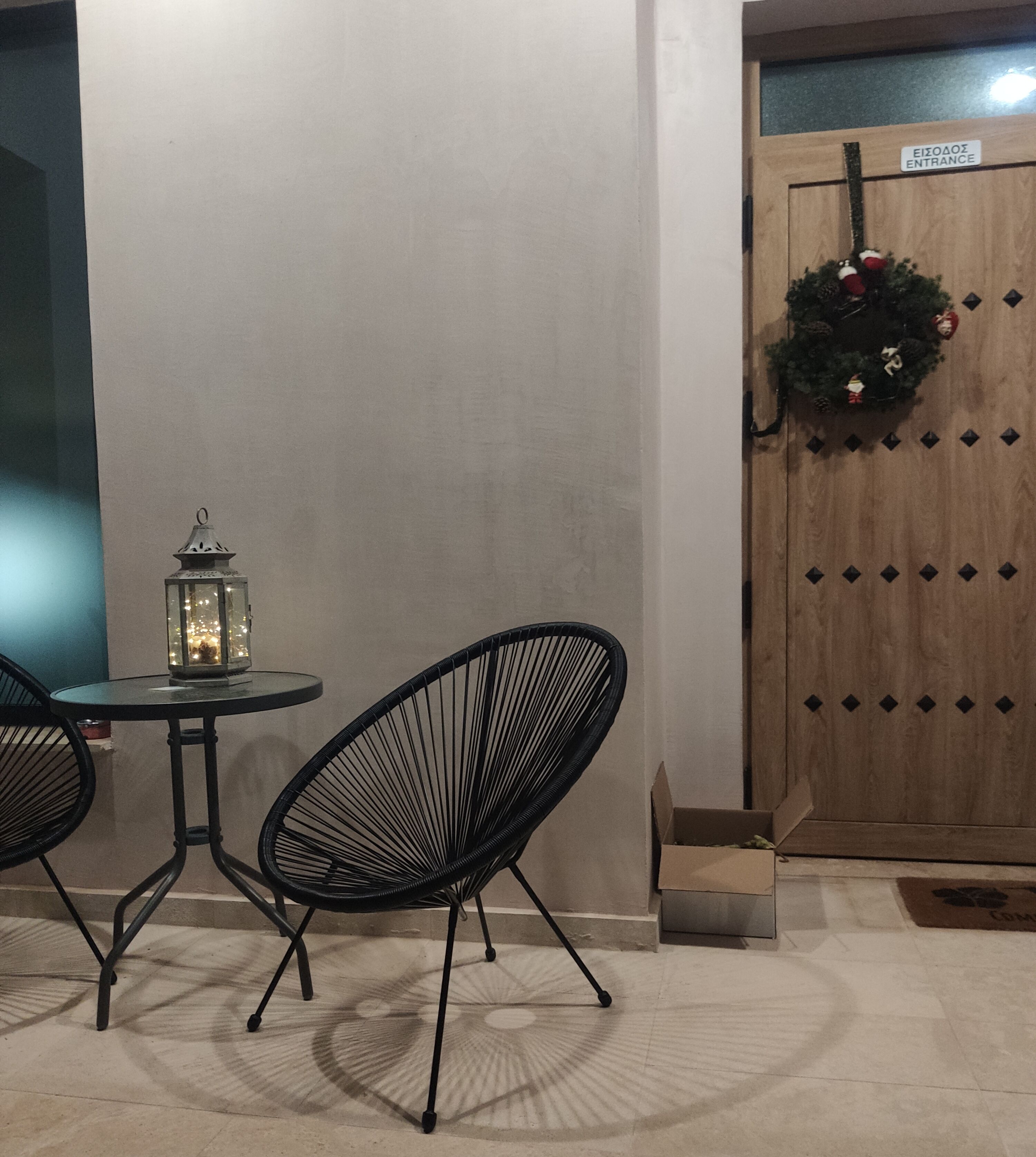 A table and two chairs outside a building with a wooden door and a wreath.
