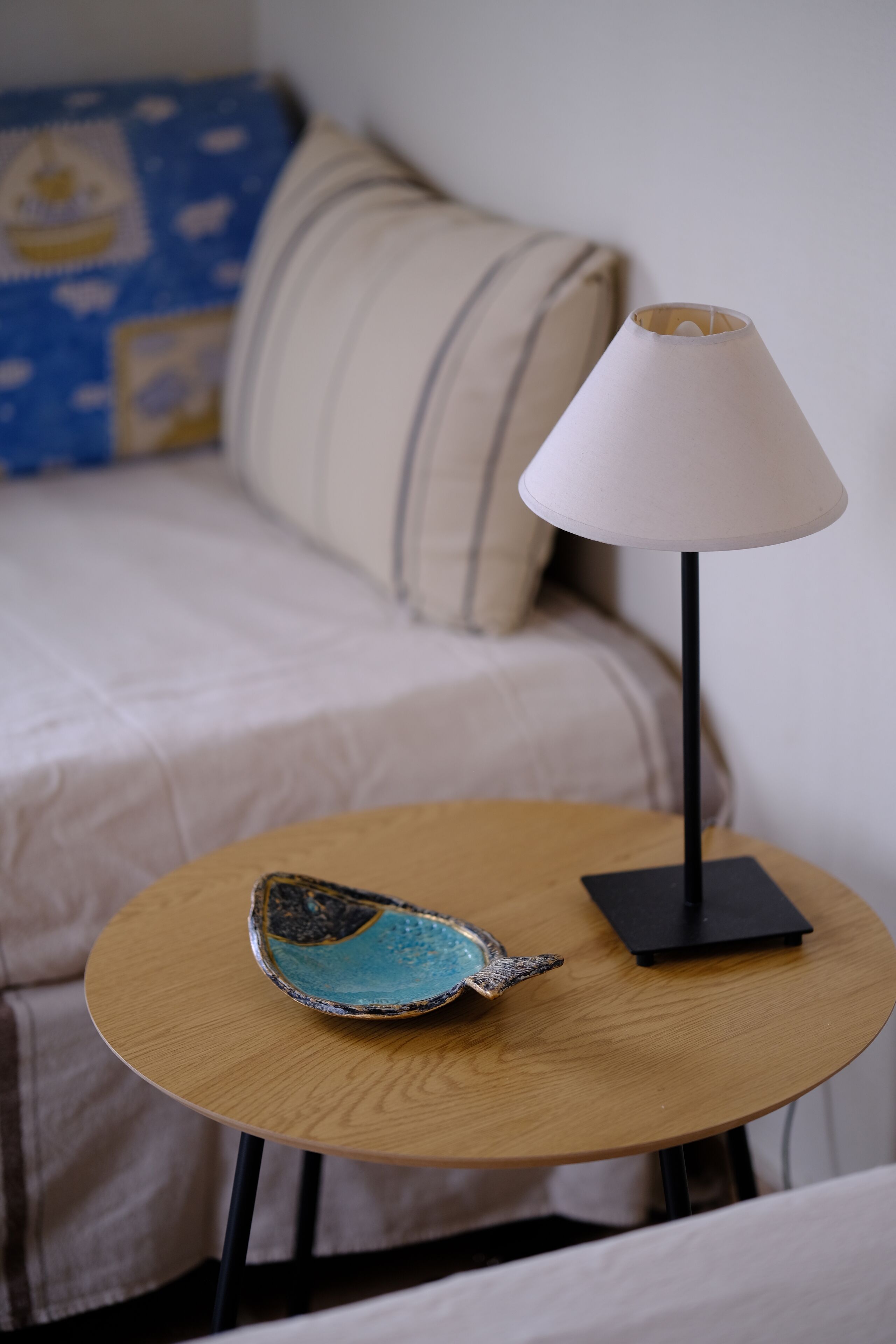 A round wooden table with a decorative ceramic piece and a black lamp.