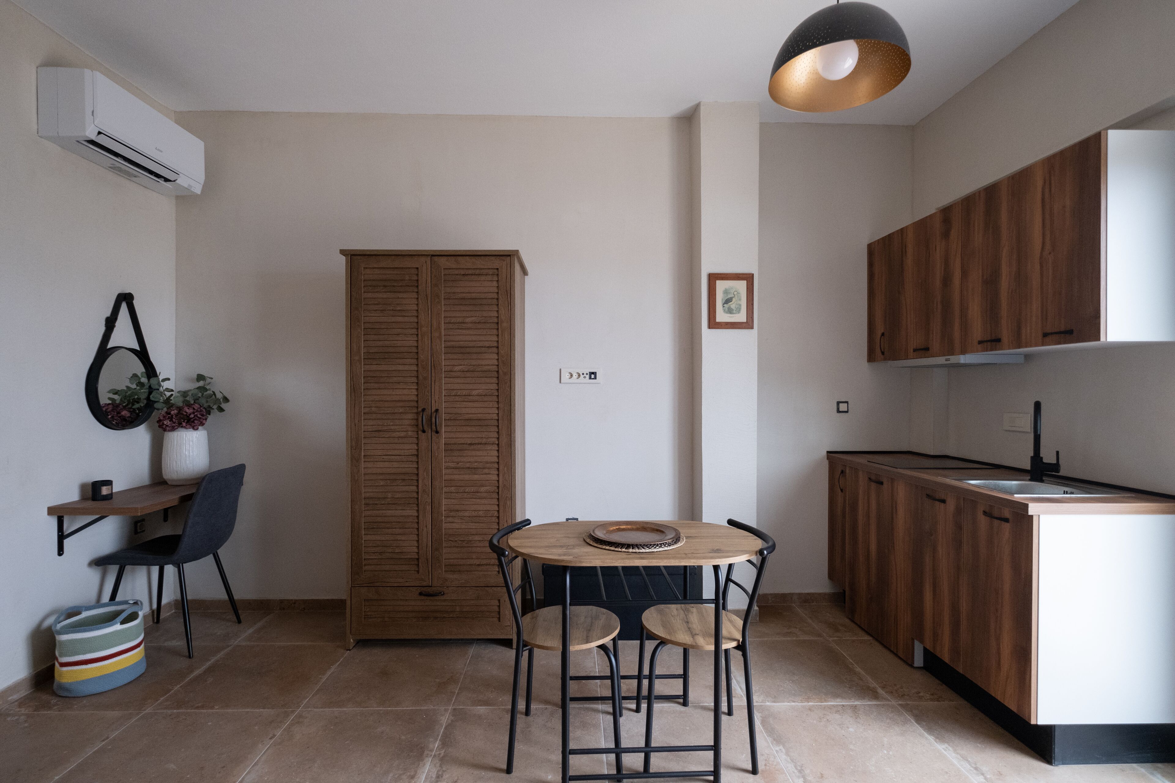 A compact kitchen with wooden cabinets, a round dining table with chairs, and a hanging pendant light.