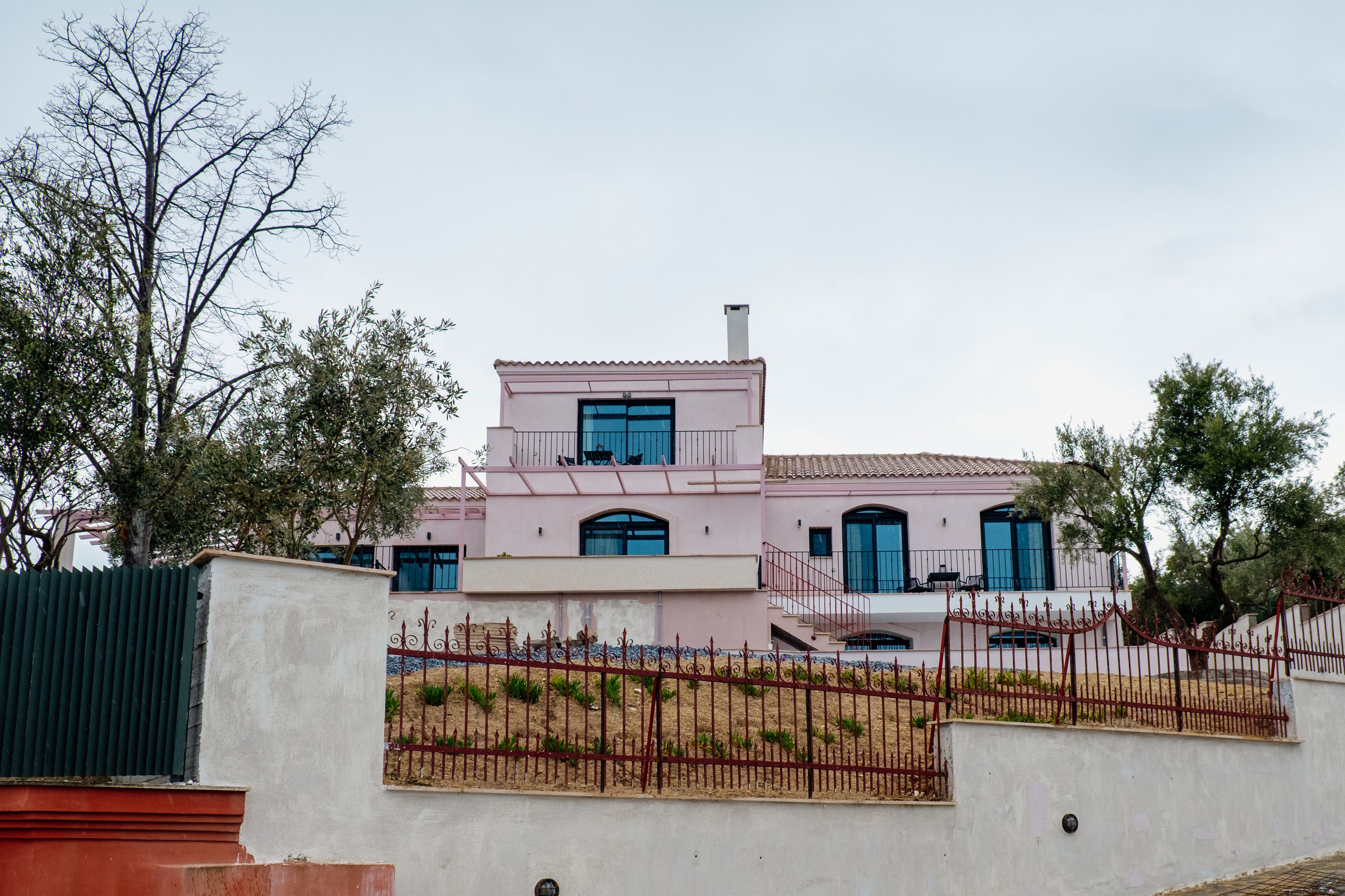 A two-story house with a pink facade, blue windows, and a red fence.