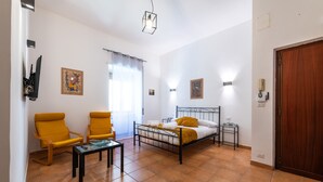 Quarto com uma cama, duas cadeiras amarelas, uma mesa pequena e obras de arte nas paredes.