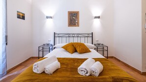 Quarto de hotel com uma cama, duas luminárias na parede, um quadro e uma pequena mesa com abajur.