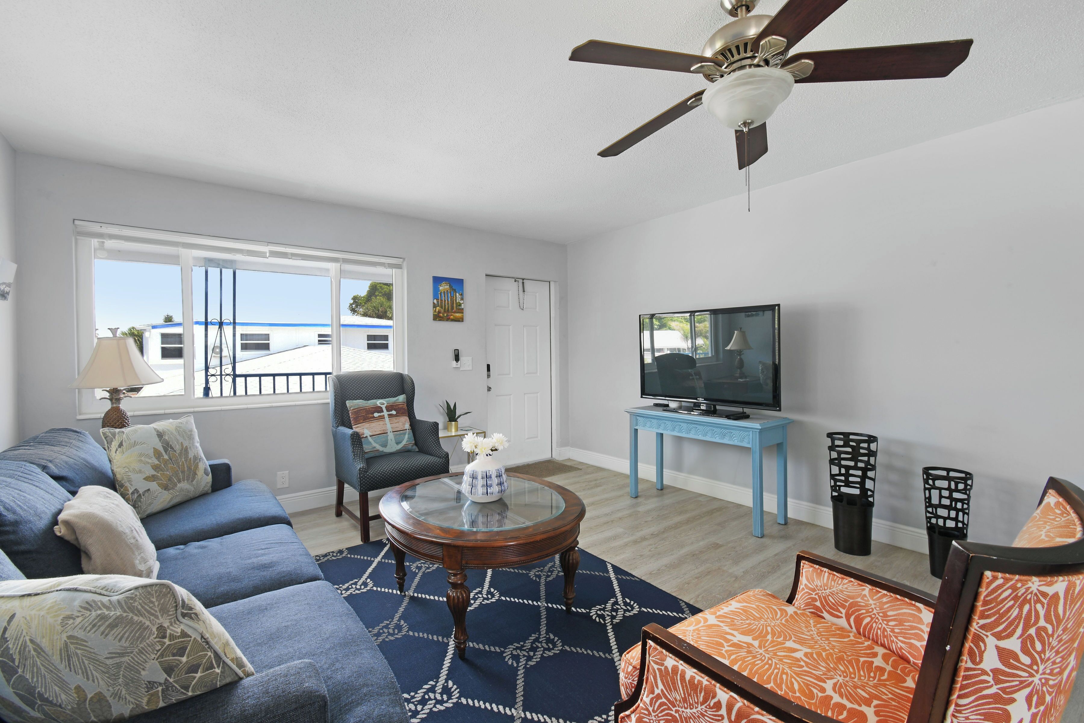 A living room with a sofa, armchair, coffee table, TV, and ceiling fan.