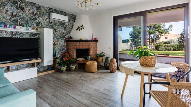 A modern living room with a flat-screen TV, a fireplace, wicker furniture, and a large window offering a view of the outdoors. - Villetta Sirena a Fontane Bianche (Syracuse)