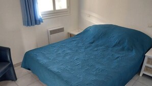 A bedroom with a bed, a chair, a heater, and a window with curtains.