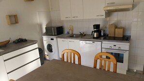 A compact kitchen with white cabinets, a washing machine, a coffee maker, and a microwave.