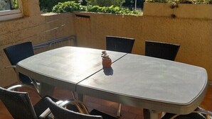 A round table with six chairs, a potted plant, and a view of a hillside with buildings.