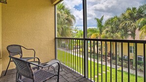 A balcony with wicker chairs, a view of a garden with palm trees, and a yellow wall. - 2 Miles to Disney Condo w/ Balcony - Pool - Gym (Kissimmee)