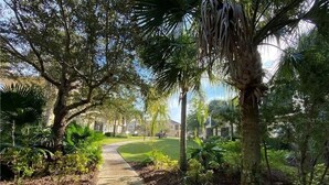 A pathway through a landscaped area with trees and shrubs. - 2 Miles to Disney Condo w/ Balcony - Pool - Gym (Kissimmee)