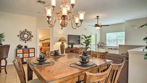 A dining area with a wooden table, chairs, and a chandelier. There is a television and a plant in the background. - 2 Miles to Disney Condo w/ Balcony - Pool - Gym (Kissimmee)
