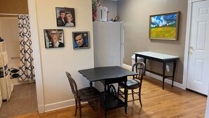 A dining area with a wooden table and chairs, a refrigerator, and wall art. - George Jones & Tammy Wynette Fan Room (Camden)