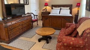 A traditional room with a wooden dresser, a bed with a headboard, a red sofa, a round wooden table, and two lamps on nightstands. - George Jones & Tammy Wynette Fan Room (Camden)