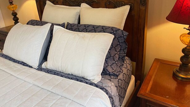 A neatly made bed with a patterned bedspread and pillows, a wooden headboard, and two bedside lamps with red shades. - George Jones & Tammy Wynette Fan Room (Camden)