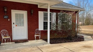A red brick building with a white door, two white metal chairs, and a covered porch. - George Jones & Tammy Wynette Fan Room (Camden)