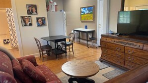 A living room with a sofa, a round table, a TV, a dresser, and a painting on the wall. - George Jones & Tammy Wynette Fan Room (Camden)