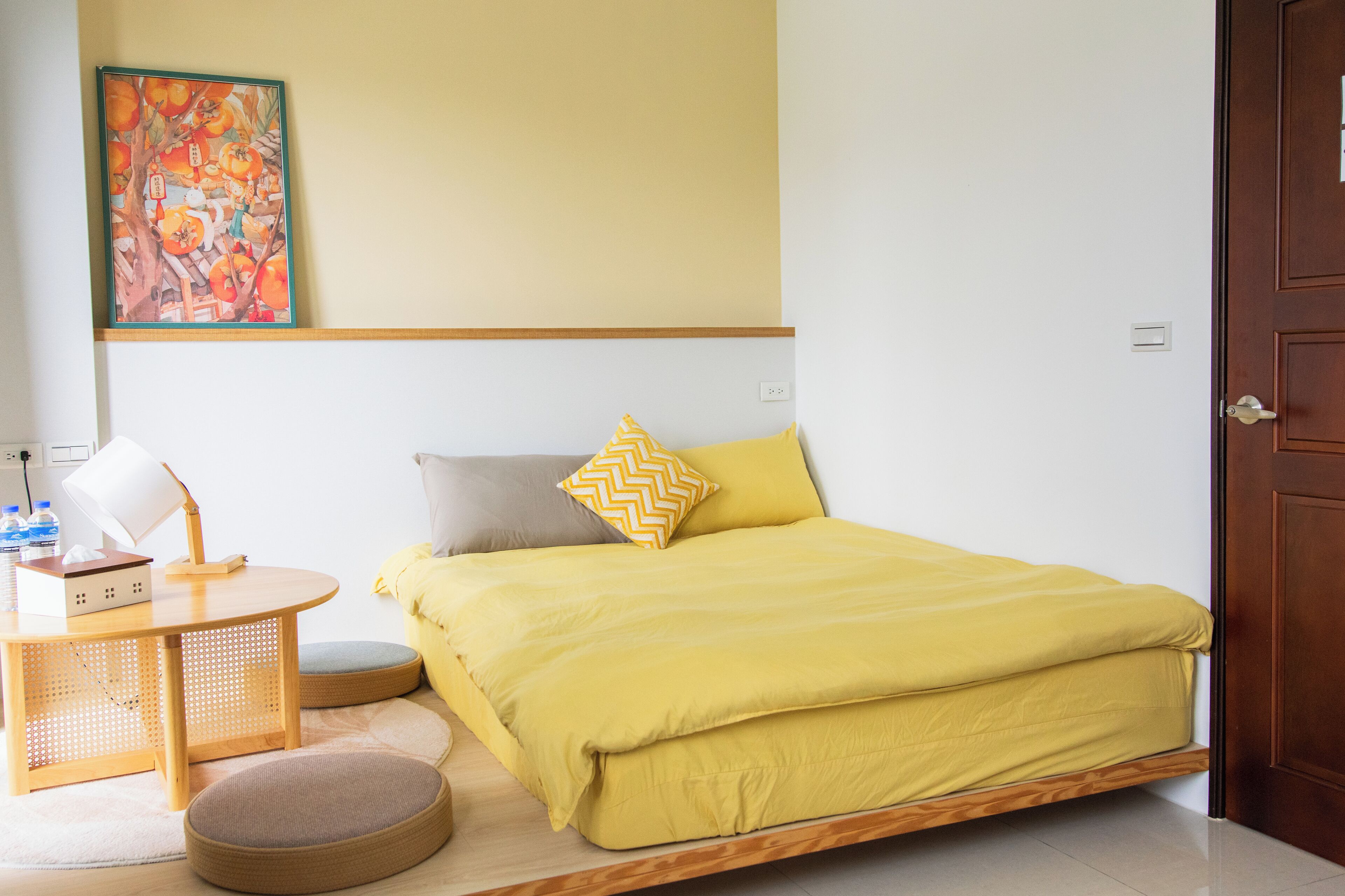Una habitación con una cama, una mesa con lámpara, una silla y un cuadro en la pared.