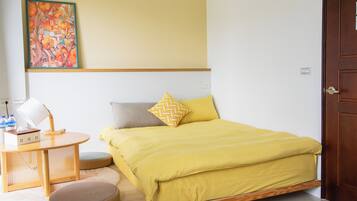 A room with a bed, a table with a lamp, a chair, and a painting on the wall.