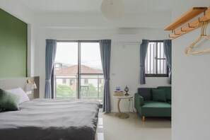 A modern hotel room with a bed, a green sofa, a small table with a lamp, and a view of the outside.
