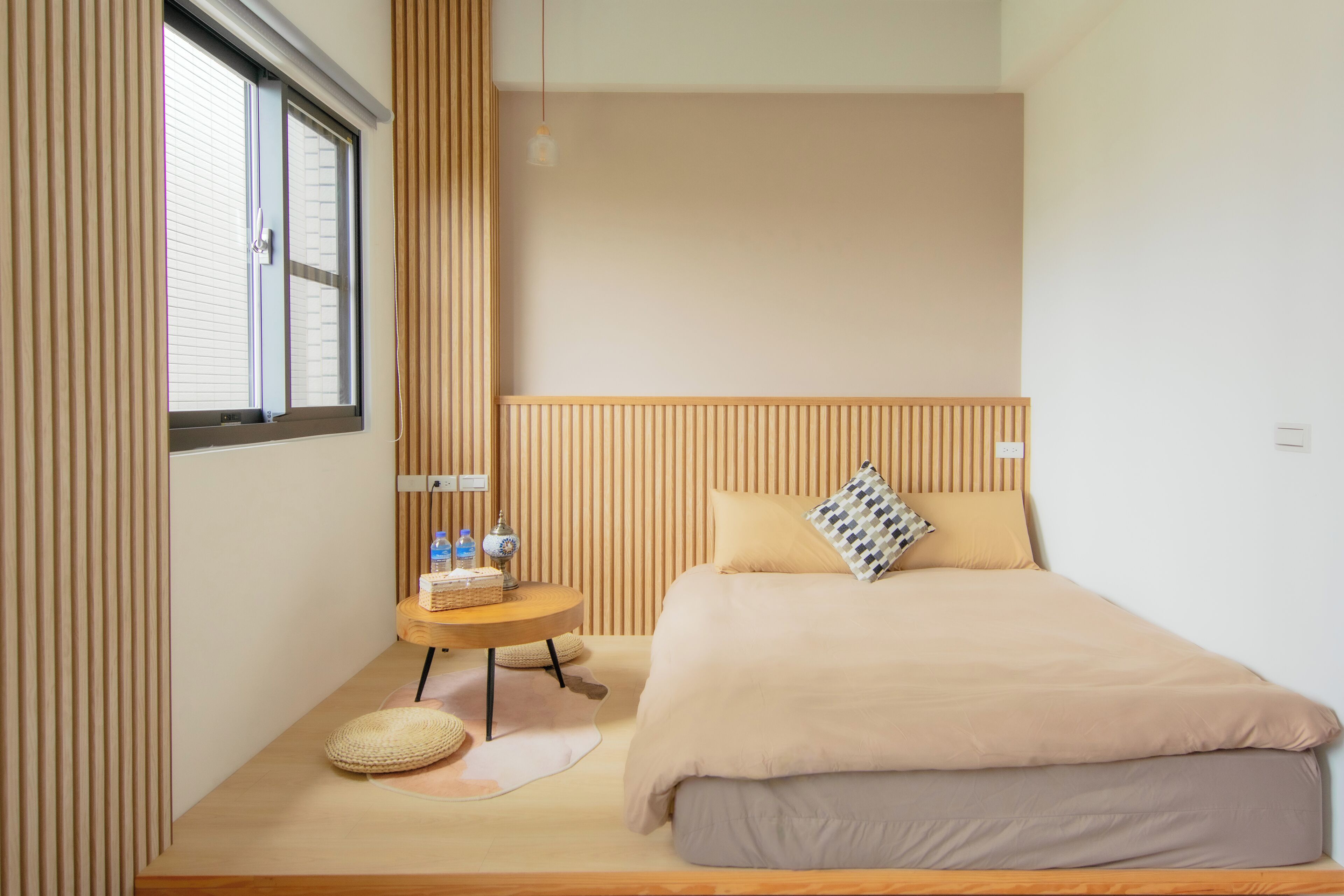Um quarto moderno com uma cama grande, uma mesinha redonda e uma janela com persianas.