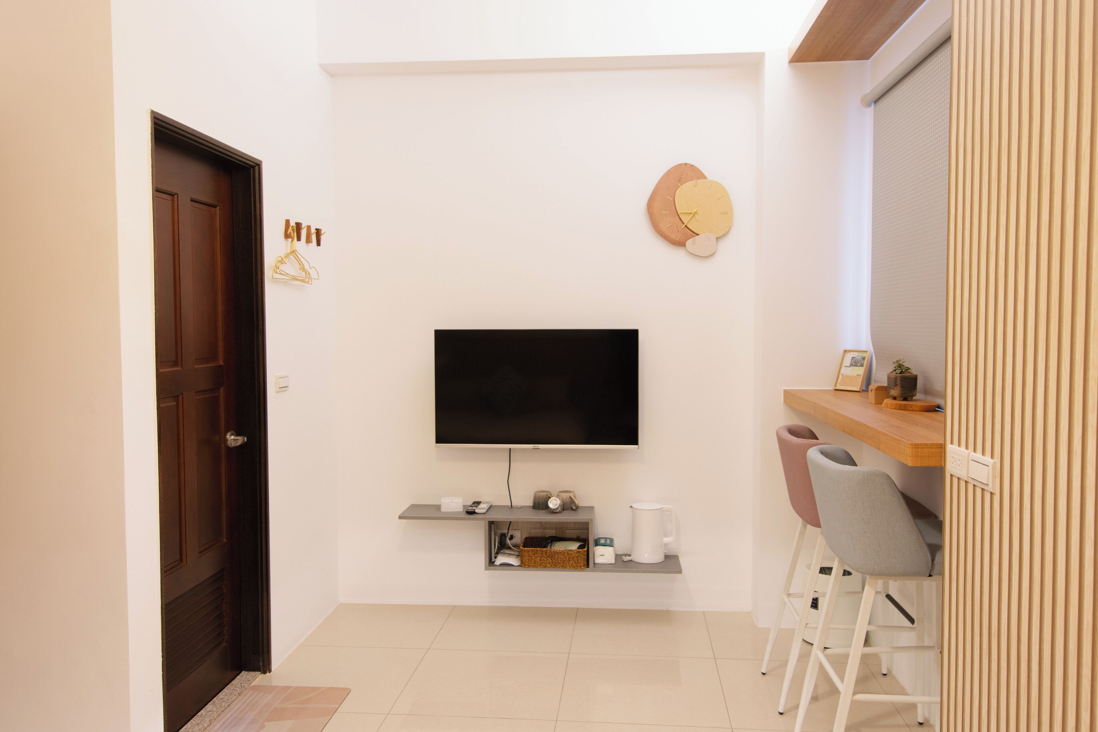 Una sala moderna con televisor de pantalla plana montado en la pared, una puerta de madera, un estante con cafetera y un área de descanso con dos sillones.