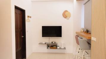Una sala moderna con televisor de pantalla plana montado en la pared, una puerta de madera, un estante con cafetera y un área de descanso con dos sillones.