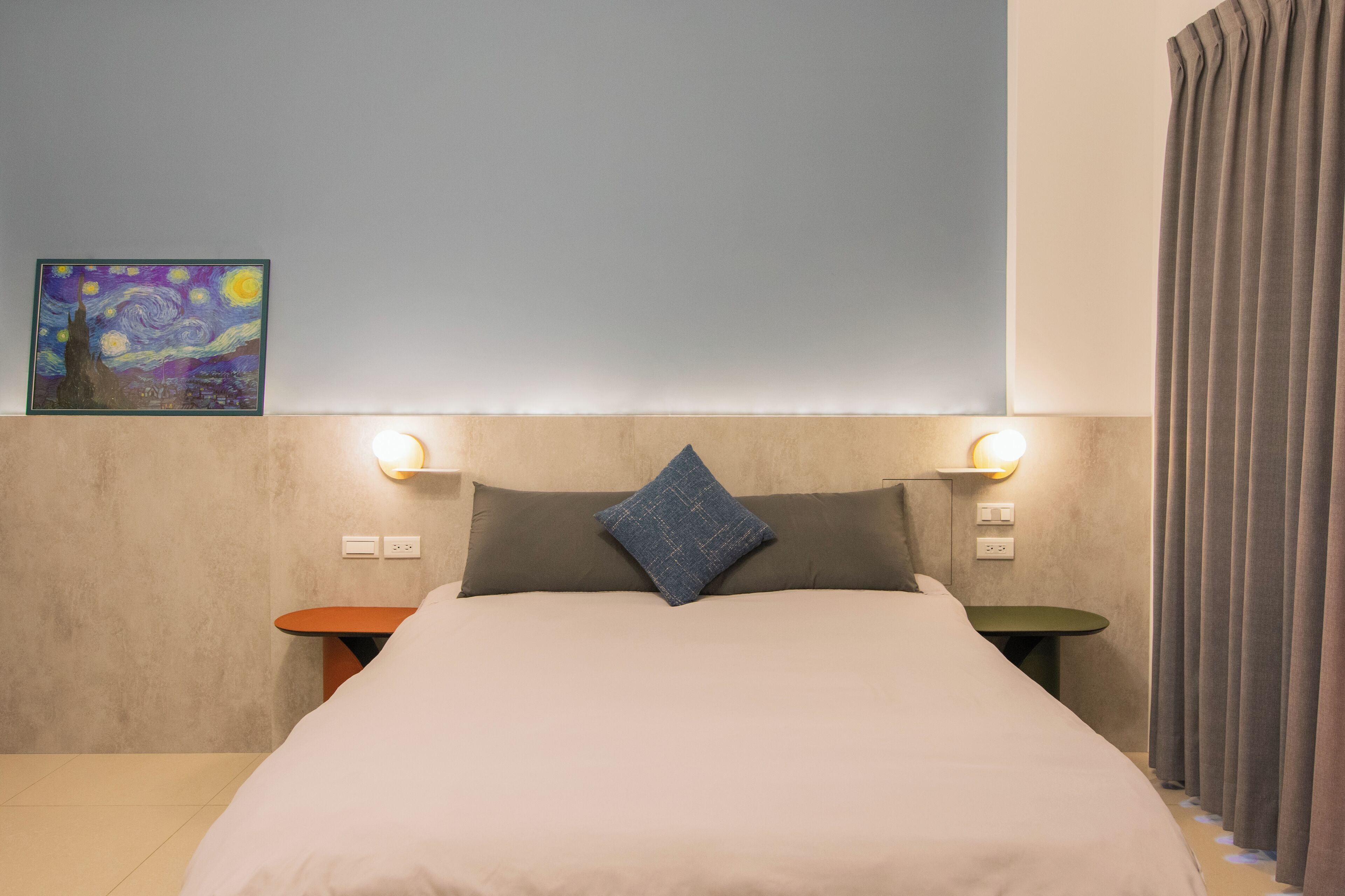 A neatly made bed with a pillow, a wall-mounted painting, and two bedside tables with wall lights.