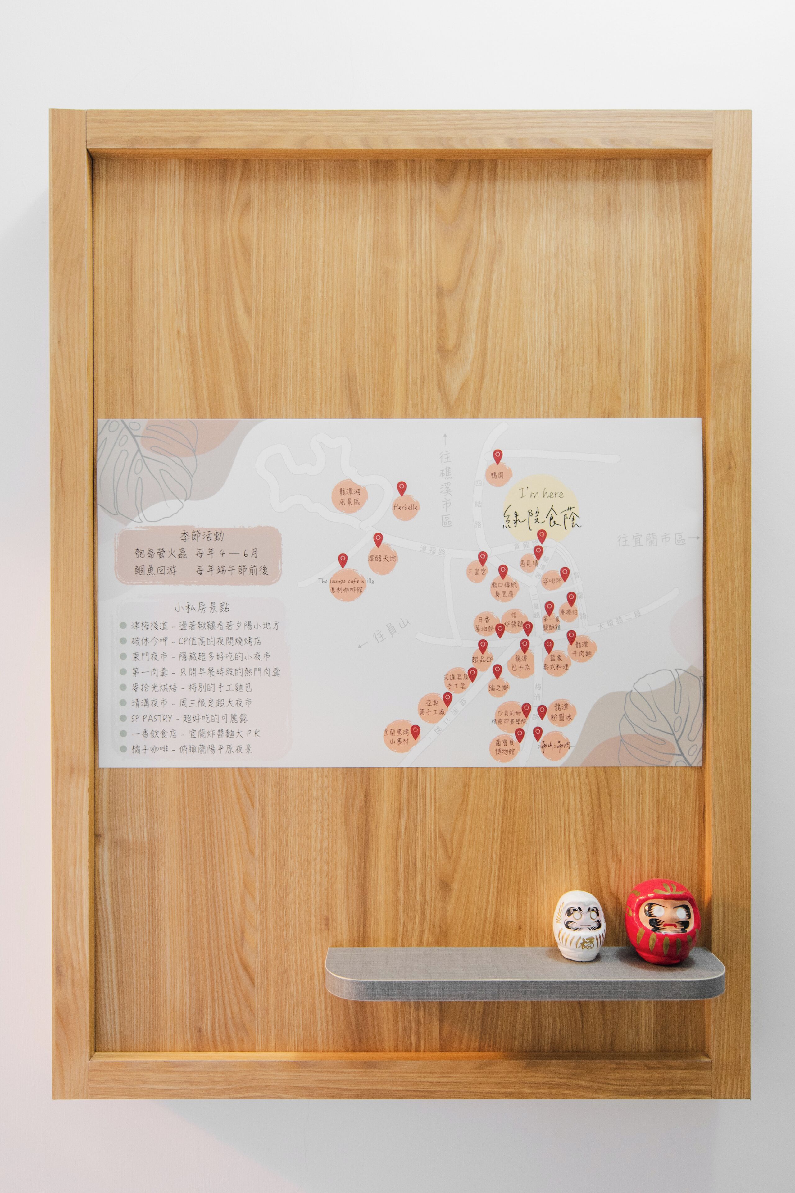 A framed map with location markers and text, a shelf with two decorative items, and a wooden frame.