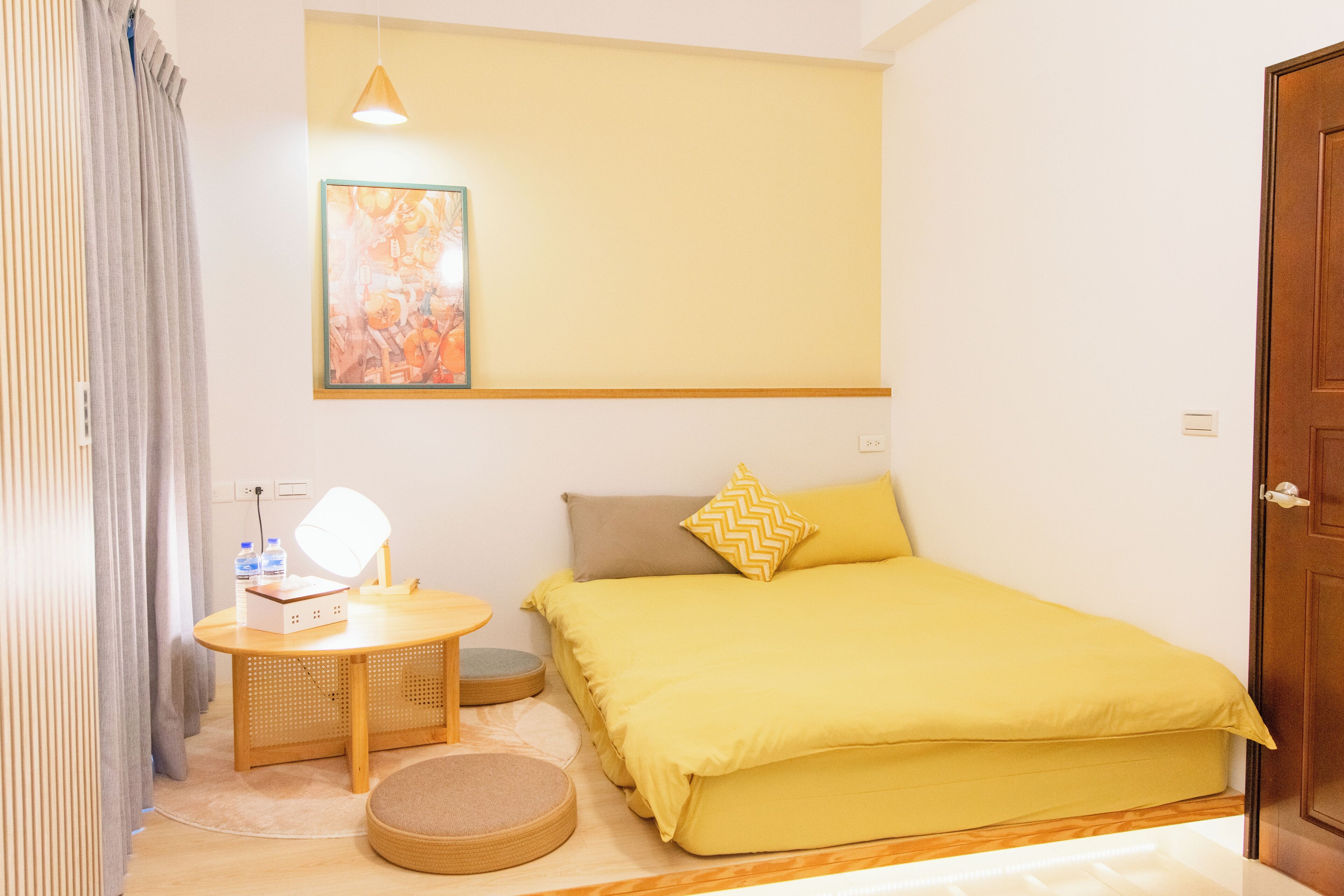 A room with a bed, a bedside table with a lamp, a small round rug, and a wall-mounted painting.