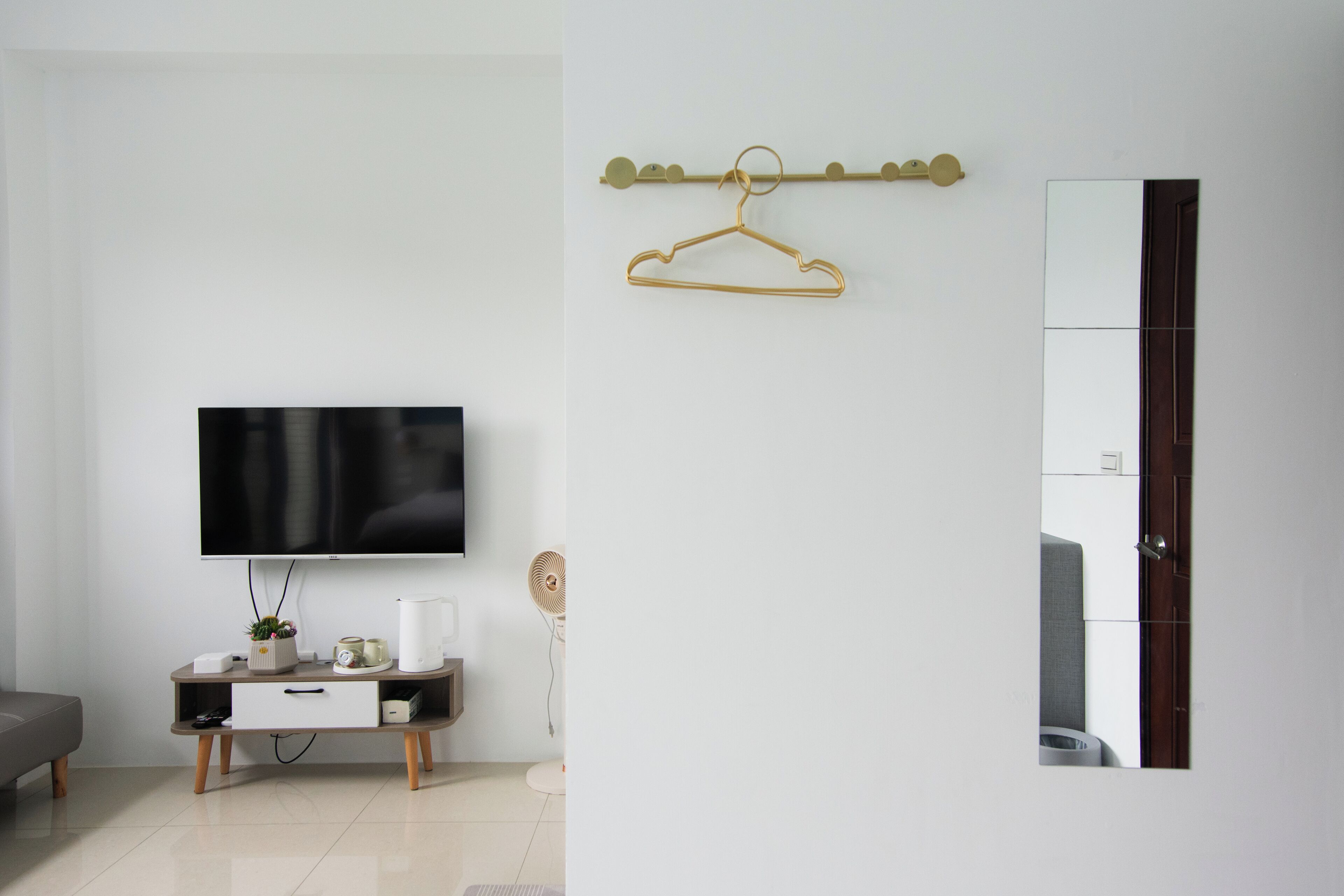 Een moderne woonkamer met een flatscreen-televisie, een houten kast, een kleine ventilator en een kapstok met één ophanger.