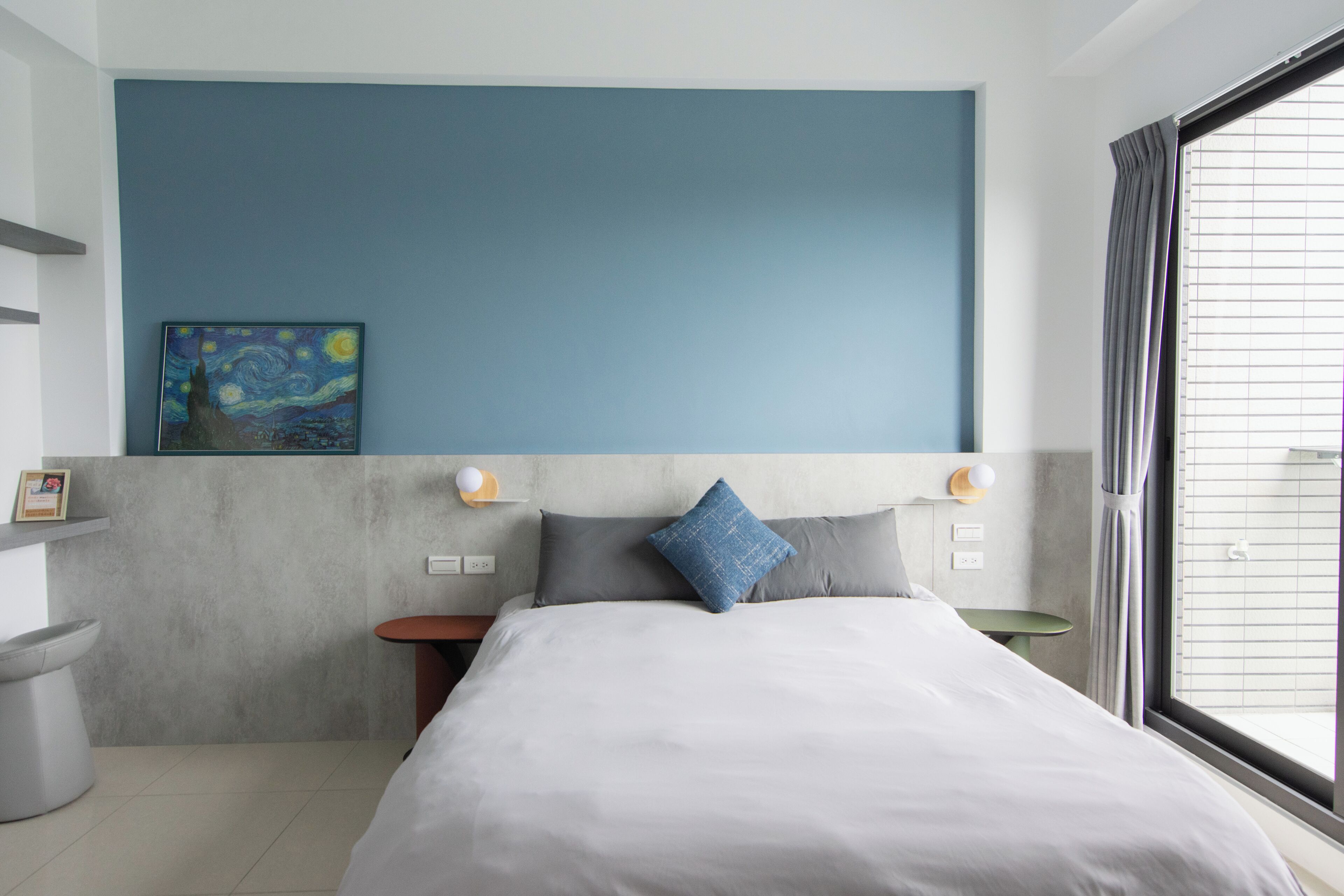 A modern hotel room with a large bed, a painting on the wall, a small table, and a window with curtains.