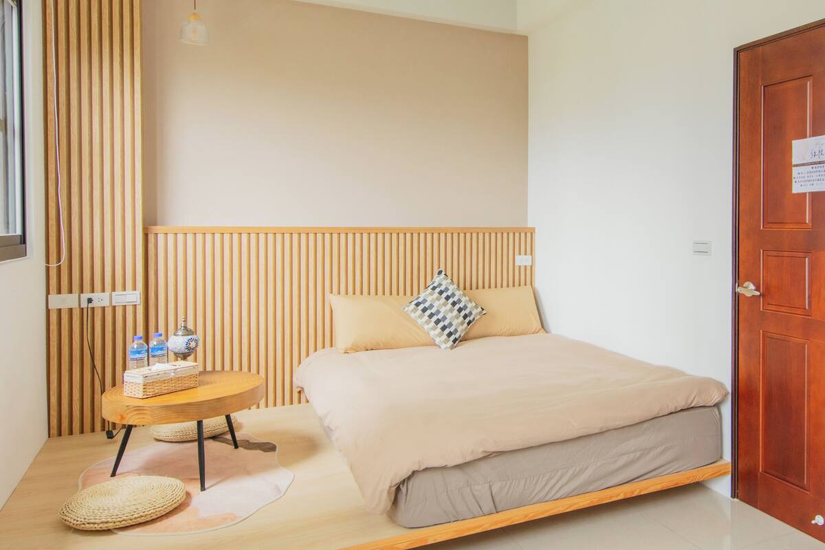 Un dormitorio con cama, mesita de noche con botellas, lámpara y cabecero de madera.