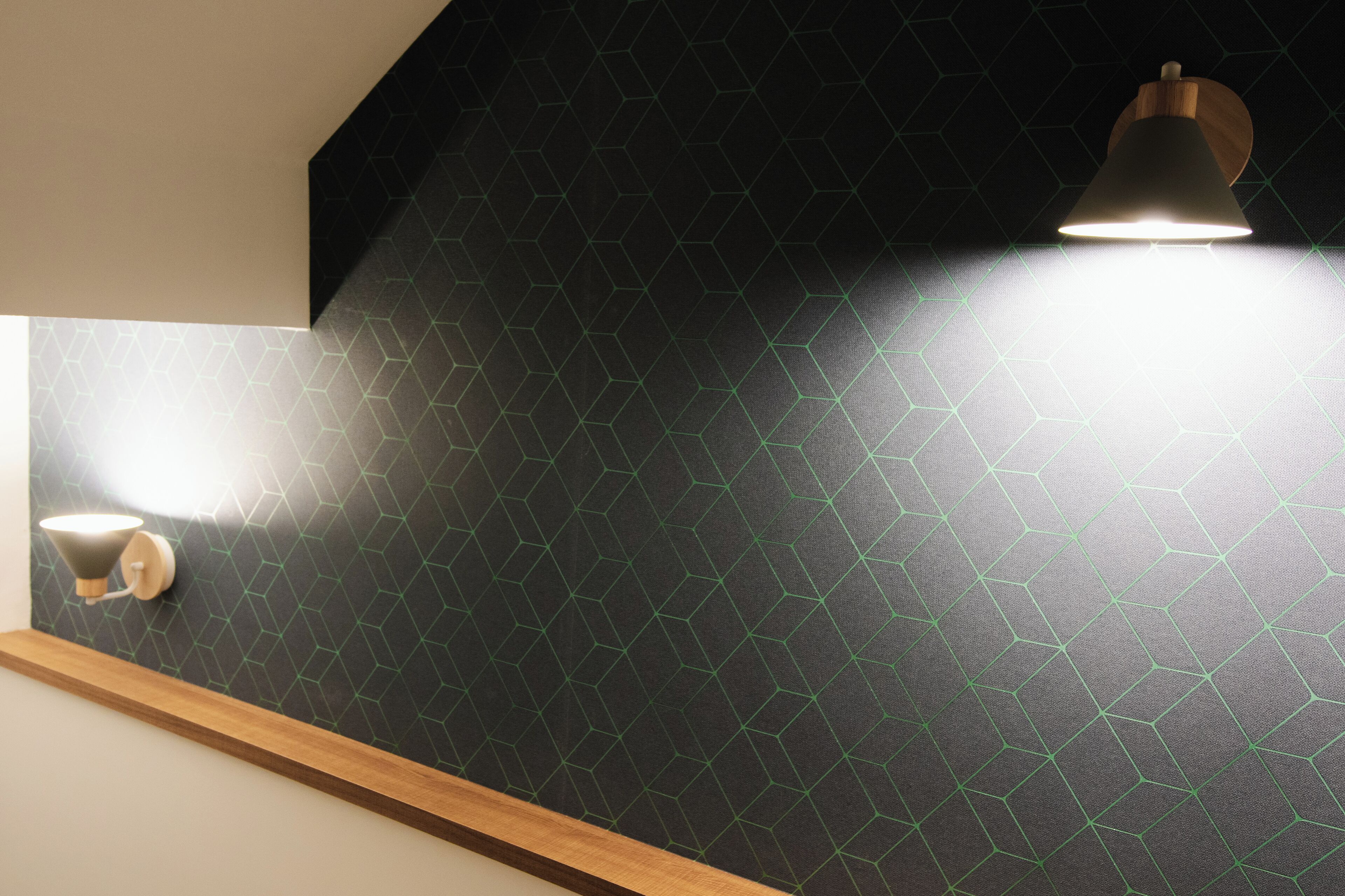 A modern interior with a geometric patterned wall, a wooden shelf, and two wall-mounted light fixtures.