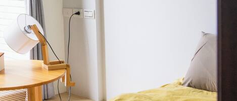 Una habitación con cama, escritorio, lámpara, un cuadro y ventana con cortinas.