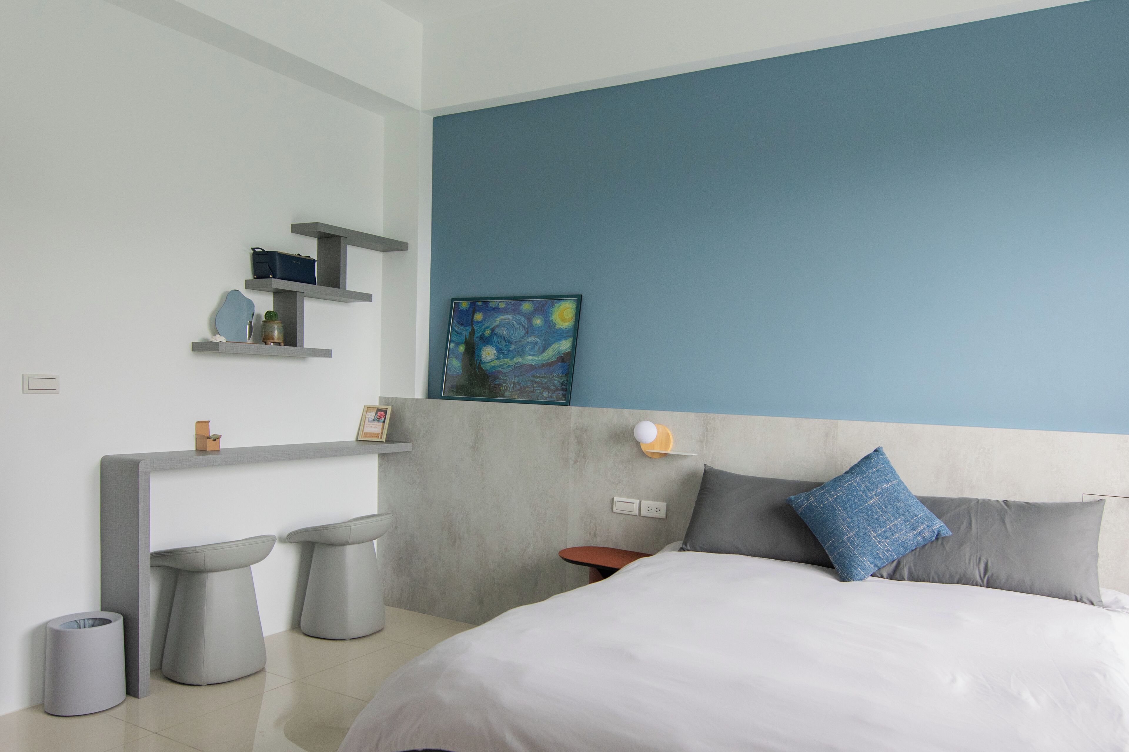Quarto moderno com cama, mesas de cabeceira, um criado-mudo e uma prateleira na parede com uma pintura.