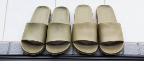 Cuatro pares de pantuflas verde oliva colocadas en orden sobre un suelo de baldosas.