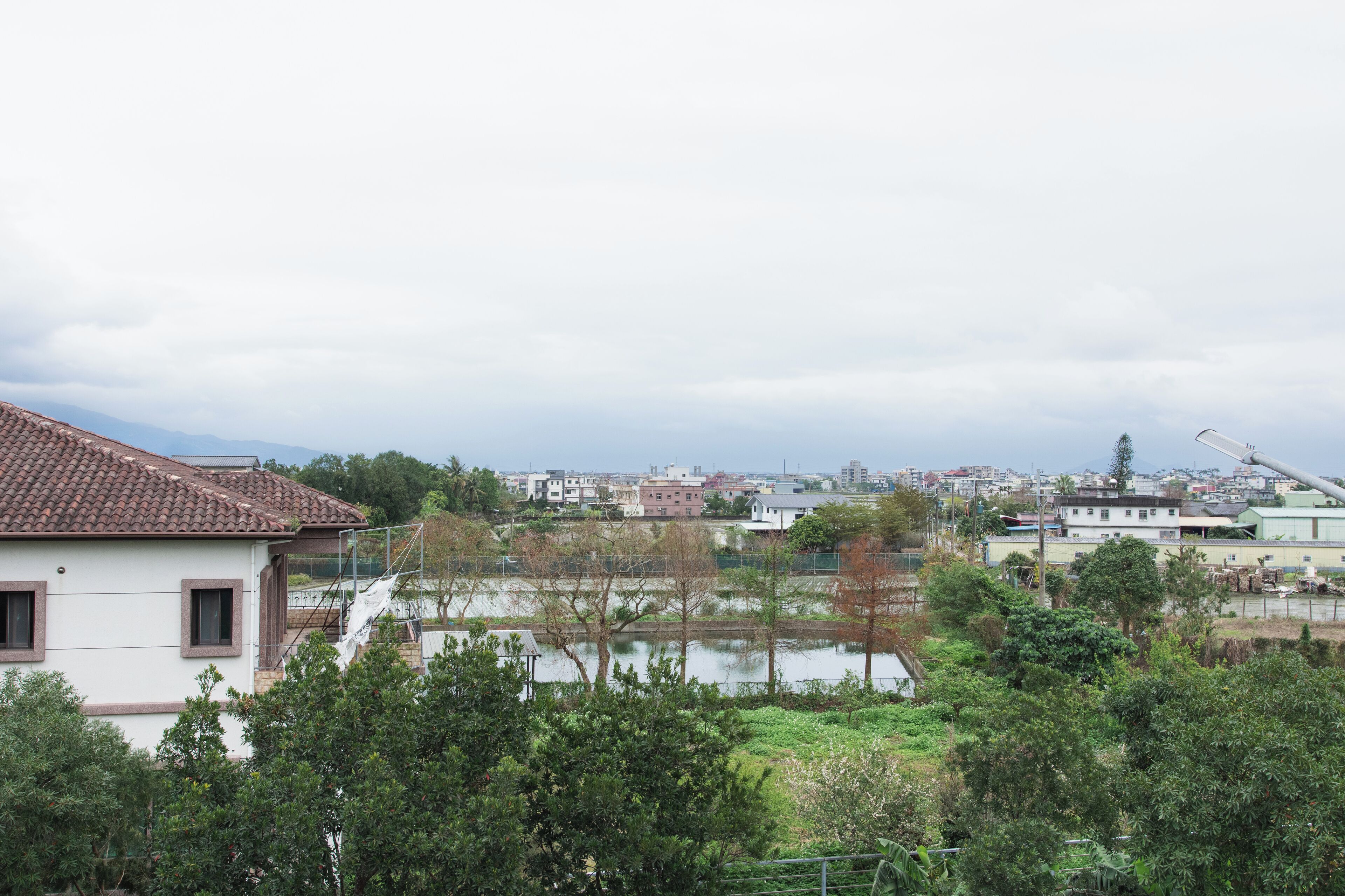 Un quartier résidentiel avec une maison dotée d’un toit en tuiles, d’un petit étang et d’un espace verdoyant environnant.